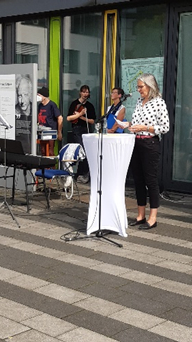 Ilka Werner steht am Pult und spricht. Passanten hören zu